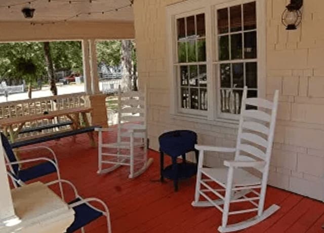 A porch with white rocking chairs and red carpet.