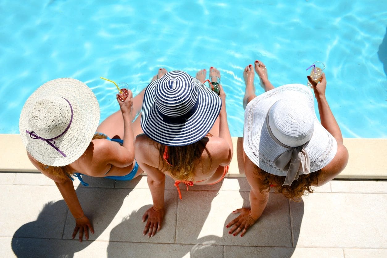 Three women sitting on the edge of a pool.