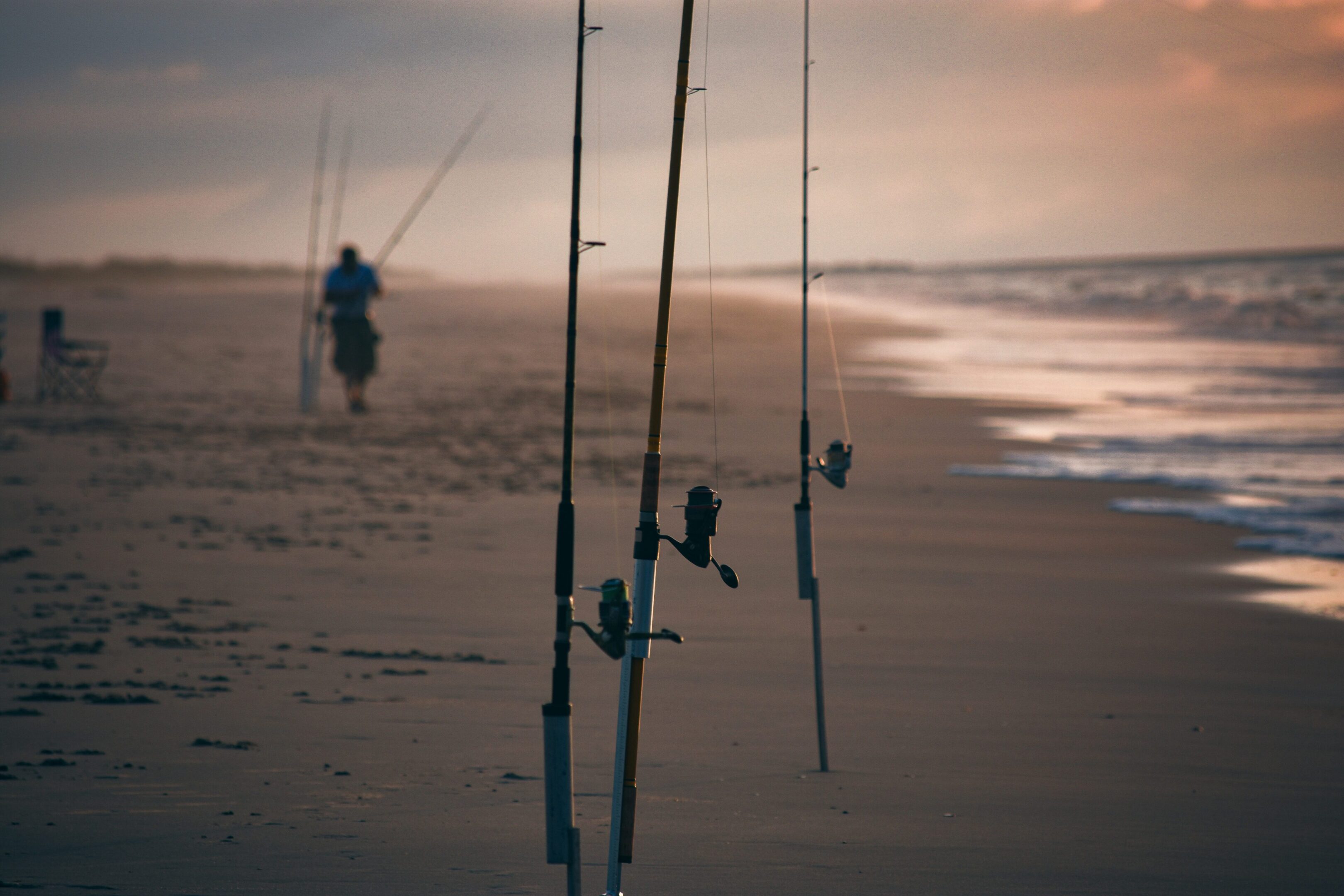 A person walking on the beach with fishing rods.