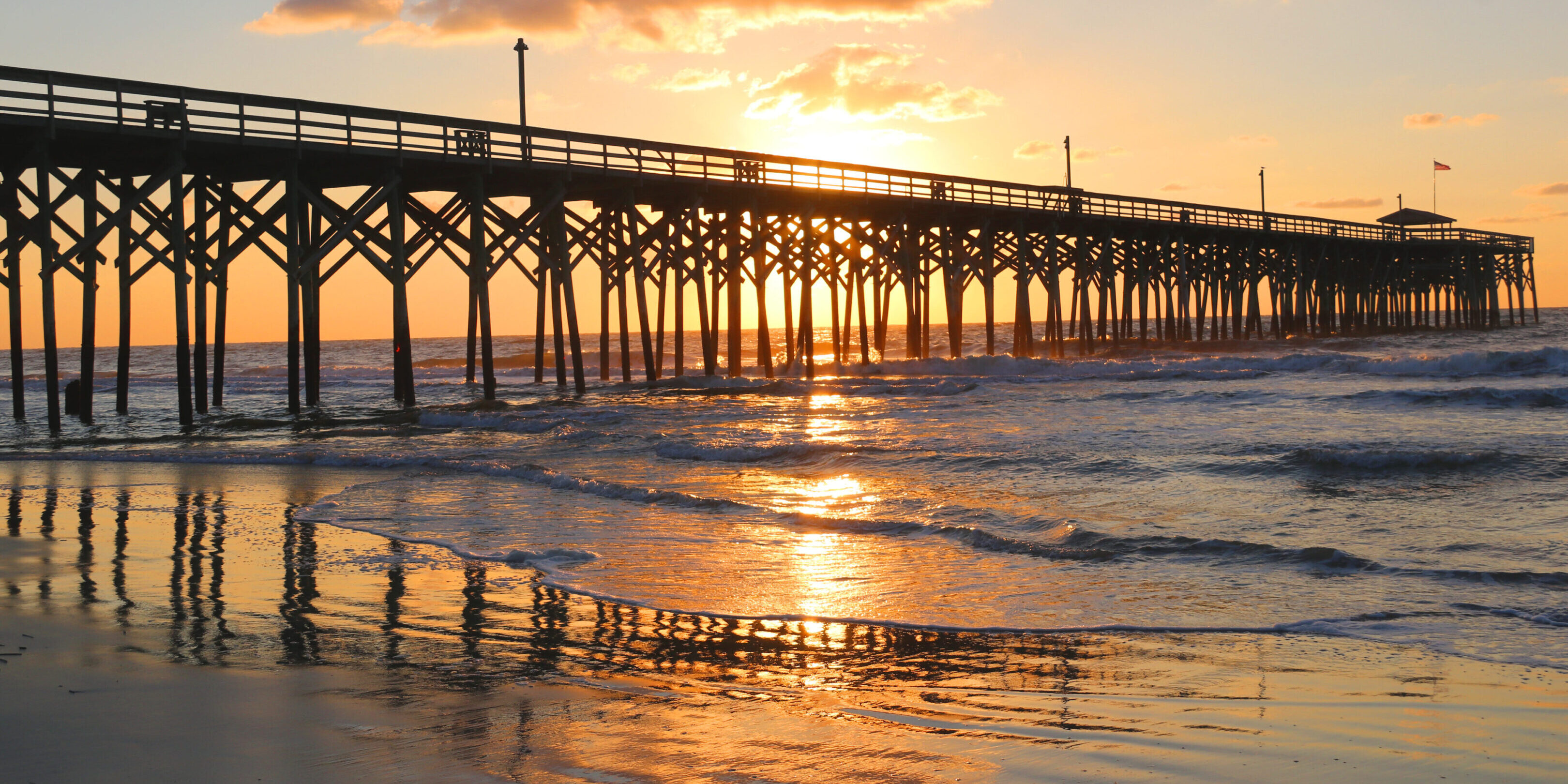 A pier with the sun setting over the ocean.